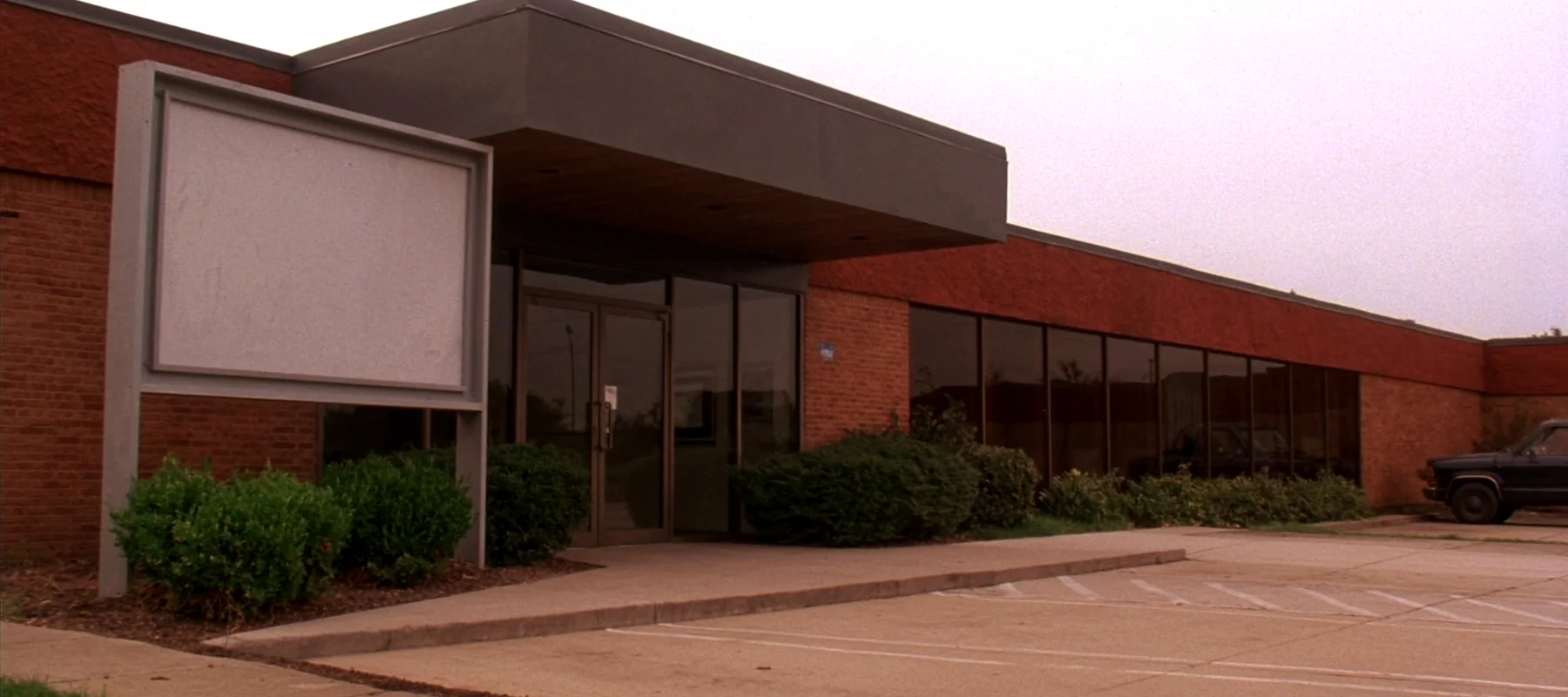 The end unit of a low brick strip building on a highway frontage road, one glass door under a metal canopy with three parking bays in front.
