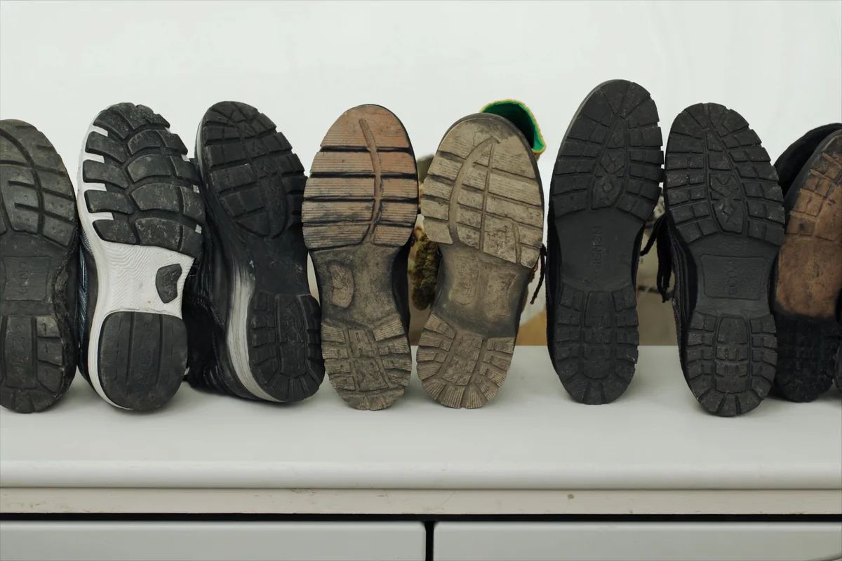 Three pairs of well worn everyday shoes lined up soles outward on a bench, each worn away in a different place.